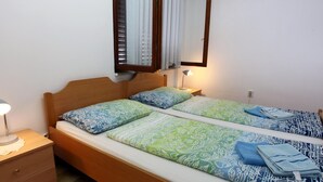 Ein Doppelbett mit gemusterten Bettbezügen, ein Nachttisch mit Lampe, ein Spiegel über dem Bett und eine kleine Kommode.