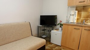 Ein kompakter Wohnbereich mit einer Couch, einem Fernseher auf einem Glastisch, einer Kaffeemaschine und einem kleinen Kühlschrank.