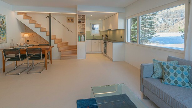 Ein modernes Interieur mit Essbereich, Treppe, Küche und einer Couch mit Kissen.