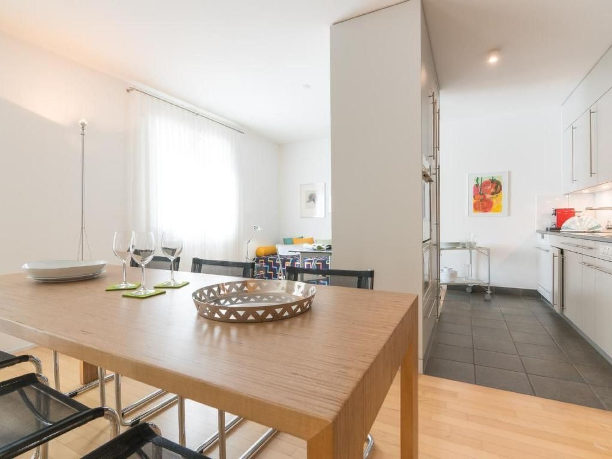 A modern kitchen with stainless steel appliances, a dining area with a wooden table and chairs, and a view of the living room.