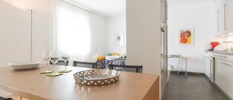 A modern kitchen with stainless steel appliances, a dining area with a wooden table and chairs, and a view of the living room.