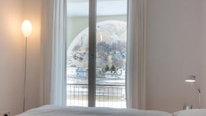 A bedroom with a large bed, a window with a view of a mountainous landscape, and a nightstand with a lamp. - Residenz Alpenrose15 by Interhome (Sils Maria)