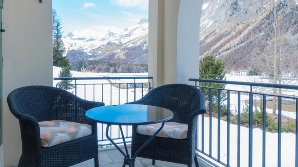 A balcony with two wicker chairs and a small table, overlooking a snowy mountain landscape. - Residenz Alpenrose15 by Interhome (Sils Maria)