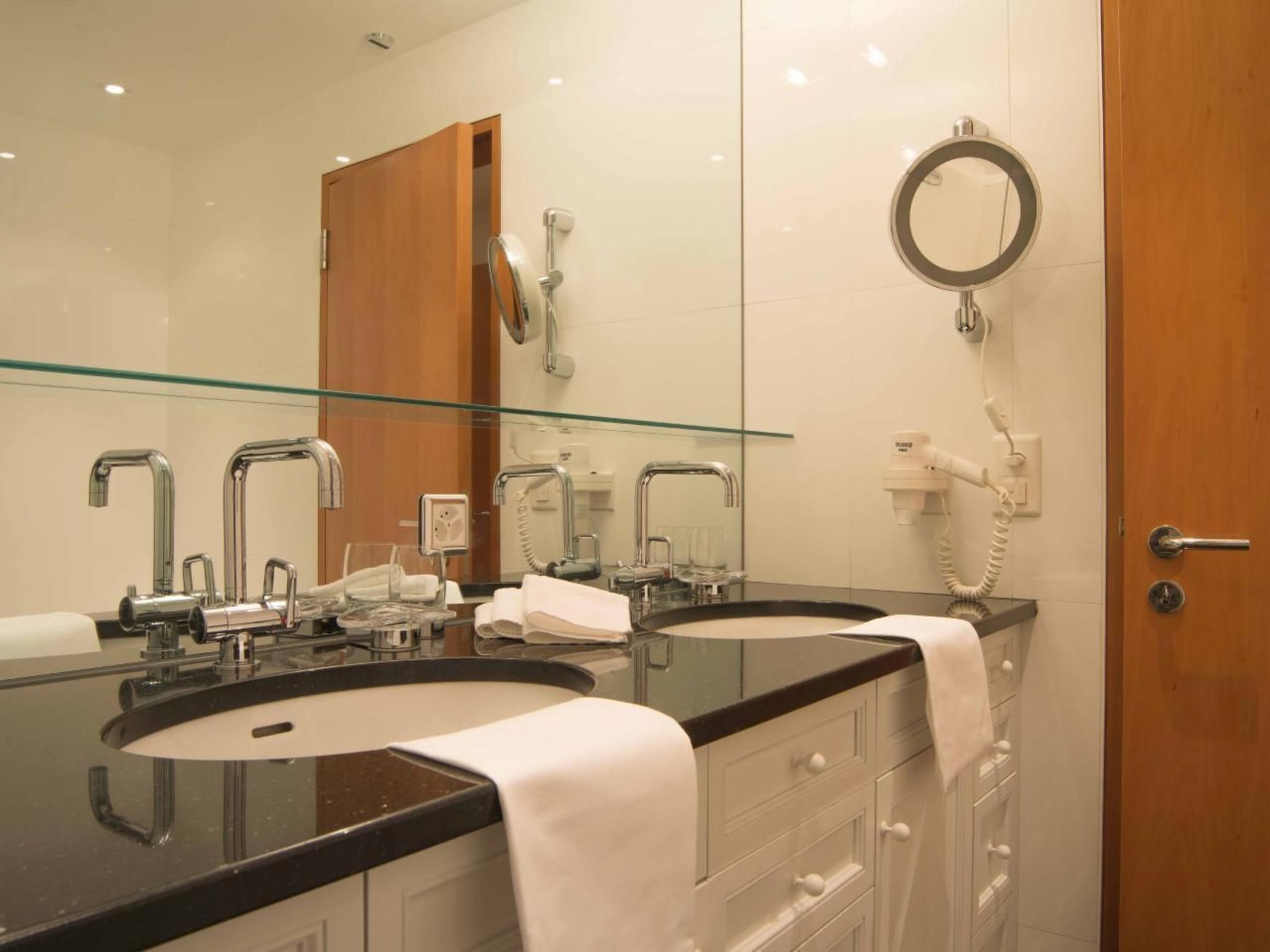 Ein Badezimmer mit zwei Waschbecken, einer Duschkabine aus Glas, einem Spiegel und einem Telefon.
