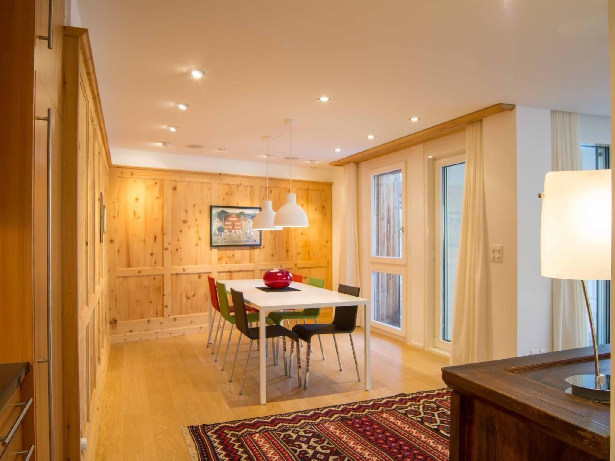 A dining area with a wooden wall, a white table, and colorful chairs.