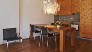 Cozinha moderna com armários de madeira, mesa de jantar com cadeiras e uma luminária pendente.