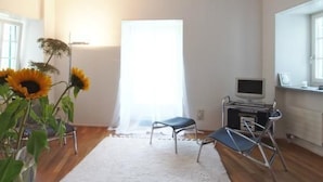 Quarto com carpete branco, uma escrivaninha com computador, uma cadeira e uma janela com cortinas.