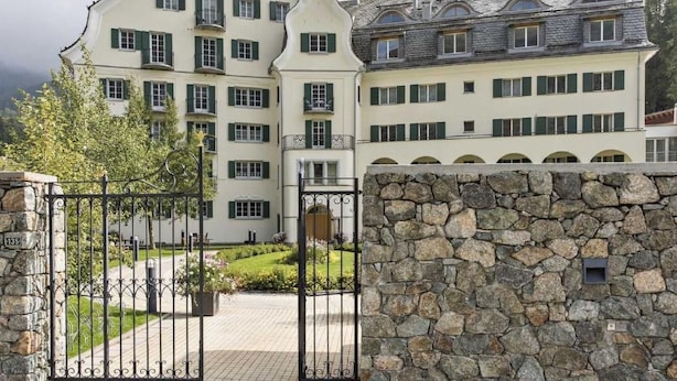 Um edifício grande, de vários andares, com fachada de pedra e entrada protegida por portão.