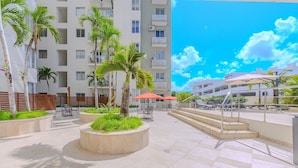 A hotel courtyard with outdoor seating, palm trees, and a staircase leading to a balcony. - Playa y Sol cercano al Aeropuerto (Boca Chica)