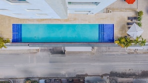 An aerial view of a swimming pool with a tiled deck, surrounded by outdoor seating and palm trees. - Playa y Sol cercano al Aeropuerto (Boca Chica)