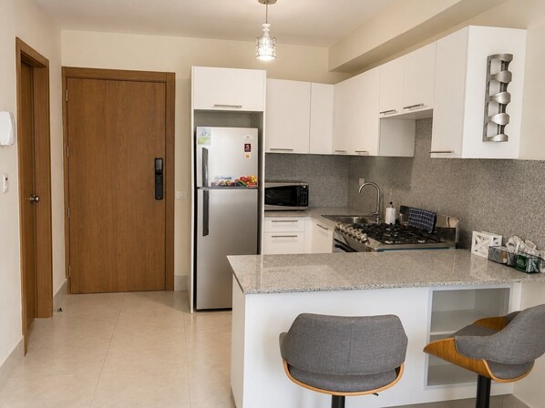 Une cuisine moderne avec des meubles blancs, un réfrigérateur en acier inoxydable, un four à micro-ondes et une cuisinière à gaz.