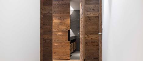 Un corridoio con rivestimenti in legno e una cucina moderna parzialmente visibile attraverso una porta aperta.