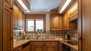 A kitchen with wooden cabinets, a window, and a tiled backsplash. - Selvas 12 by Interhome (Sils Maria)