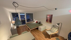 Une chambre à coucher de taille modeste, comprenant un lit, un bureau, une chaise, une lampe sur pied et un tableau accroché au mur.