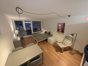 A compact bedroom with a bed, a desk, a chair, a floor lamp, and a painting on the wall. - Apartment Barga by Interhome (Davos)