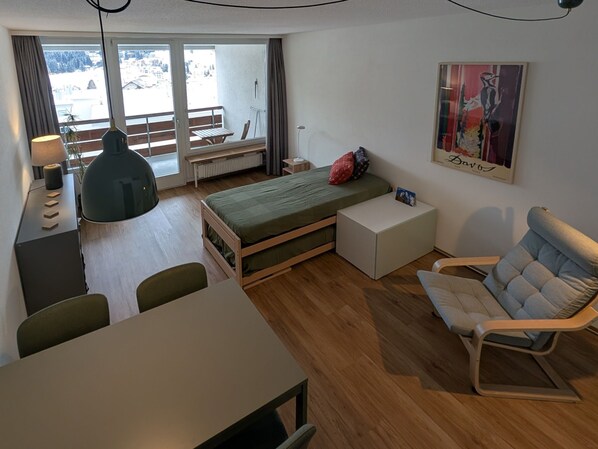 Une chambre à coucher de taille réduite, comprenant un lit, une table de chevet, une chaise, un bureau et une vue sur l’extérieur.