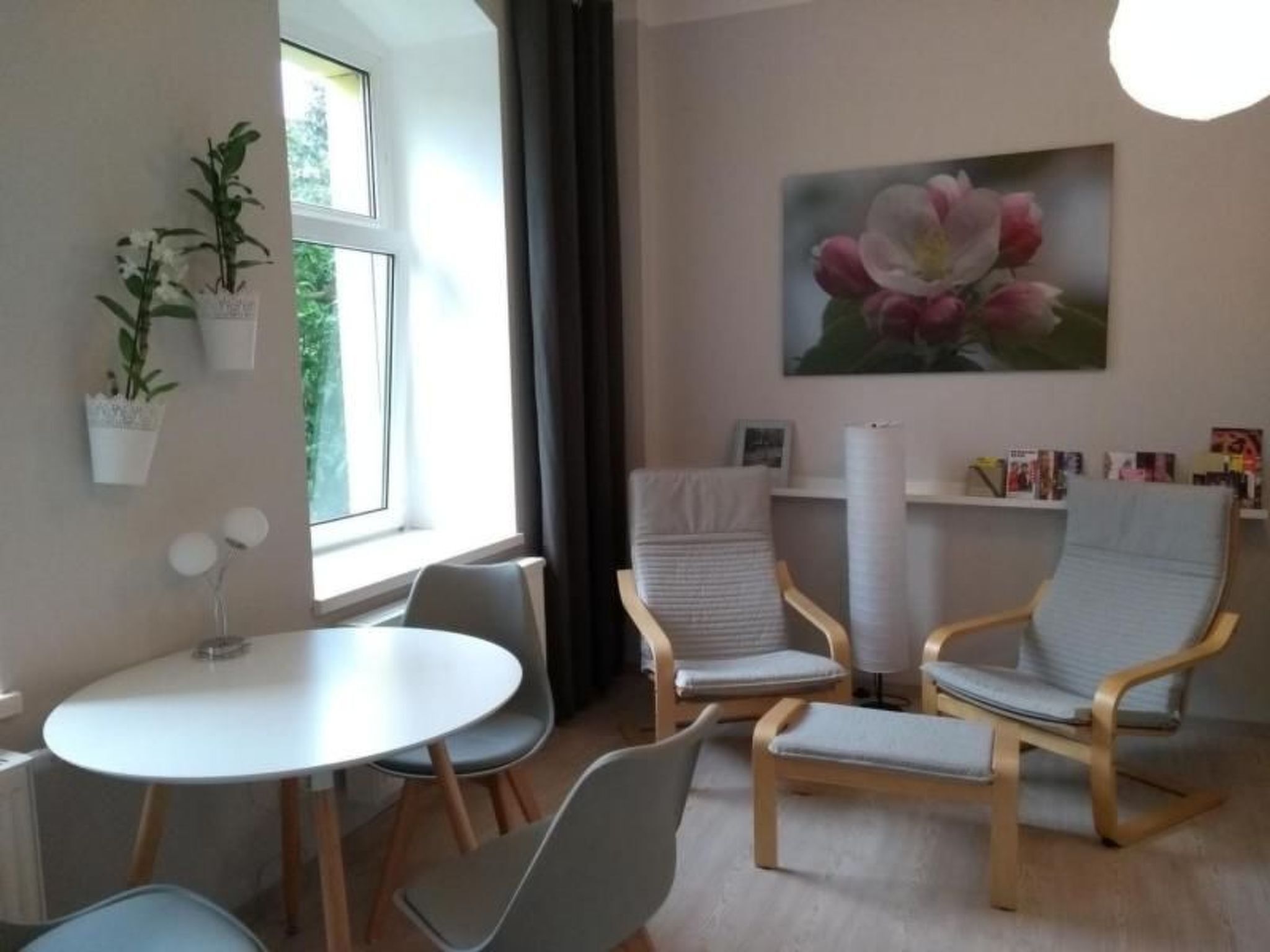 A modern room with a round table, two chairs, a bookshelf, and a window with curtains.