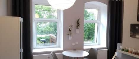 A modern kitchen with a dining area, large windows, and a hanging light fixture.