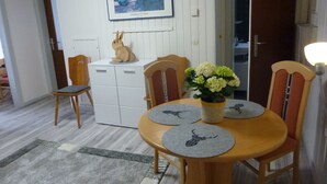 Ruokailutilassa on puinen pöytä, tuoleja, valkoinen kaappi, jänisaiheinen veistos ja seinällä oleva kehystetty kuva.