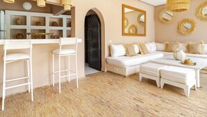 Un salon moderne avec un canapé blanc, un coin repas avec des chaises blanches et une cuisine dotée d’étagères remplies de poteries.