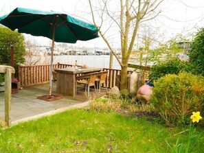 Eine Holzterrasse mit Tisch und Stühlen, einem Sonnenschirm und Blick auf Boote im Hintergrund.