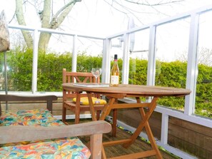 Eine überdachte Terrasse mit Holztisch und -stühlen, einer Weinflasche und einem Buch.