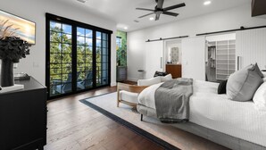 Una camera da letto moderna con un letto grande, una scrivania e vista sul verde attraverso ampie finestre a tutta altezza.