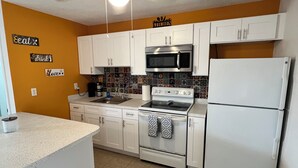 A kitchen with white cabinets, a microwave, stove, and refrigerator. There are decorative tiles on the backsplash and a ceiling fan. - Casita Cortes is quiet, cozy and centrally located in Tampa. (Tampa)