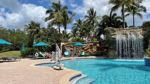 Una piscina con una cascada, rodeada de palmeras y sillones de descanso.