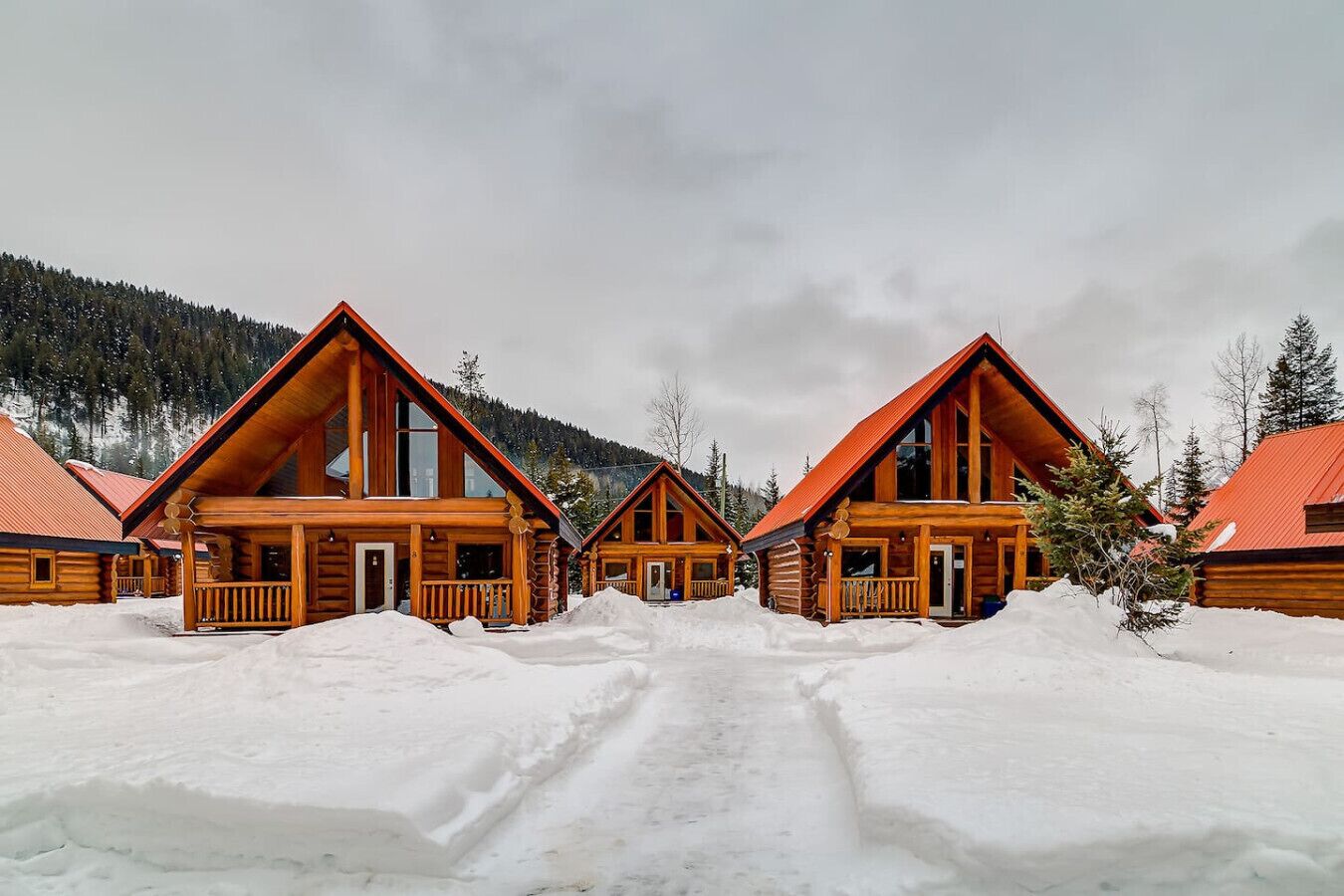Une rangée de chalets en bois, avec un paysage enneigé et des montagnes en arrière-plan.