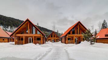 Une rangée de chalets en bois, avec un paysage enneigé et des montagnes en arrière-plan.