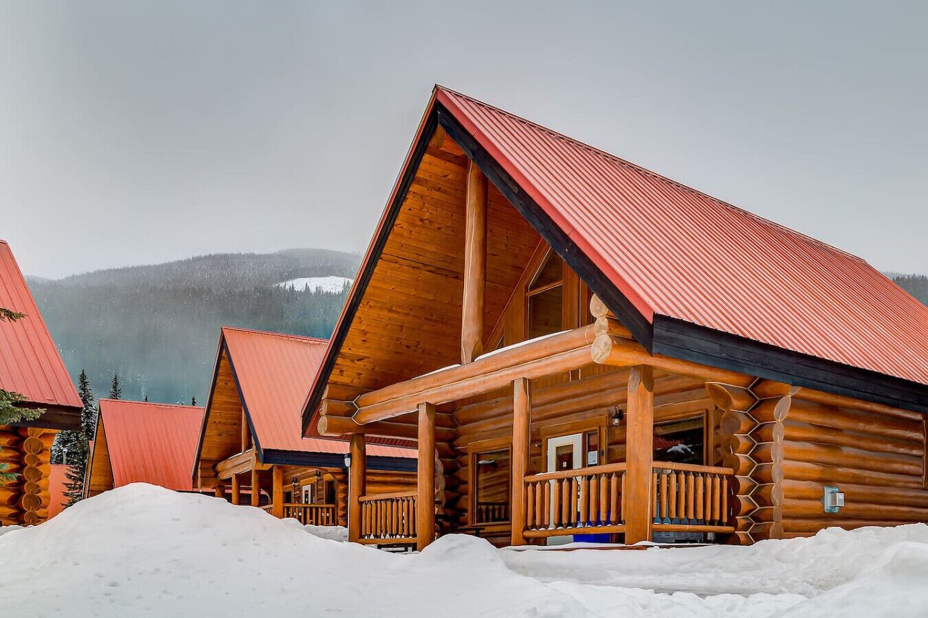 A log cabin with a red roof and wooden exterior, surrounded by snow.