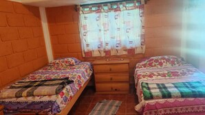 A small, cozy room with two wooden beds, a wooden dresser, and a window with patterned curtains. - Perfect 1-bedroom house in enchanting Tepoztlán for your getaway (Tepoztlán)