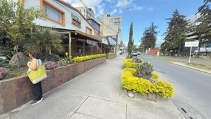 Un hôtel à l’architecture moderne, avec un restaurant bien visible et un trottoir bien entretenu agrémenté de parterres de fleurs.
