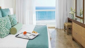 Habitación de hotel con cama, bandeja de desayuno, cómoda y vista al océano.