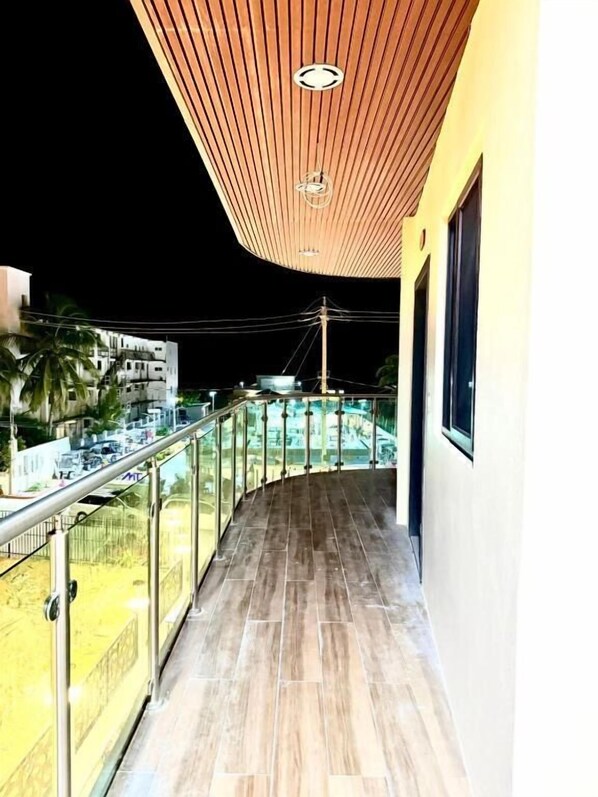 A balcony with a wooden ceiling, glass railings, and a view of buildings and palm trees. - HOTEL SEA QUEEN SUITE & GOLF CART RENTAL (San Pedro)