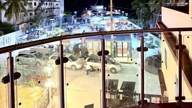 Un balcón con vista a una calle concurrida de noche, que incluye coches estacionados y edificios.