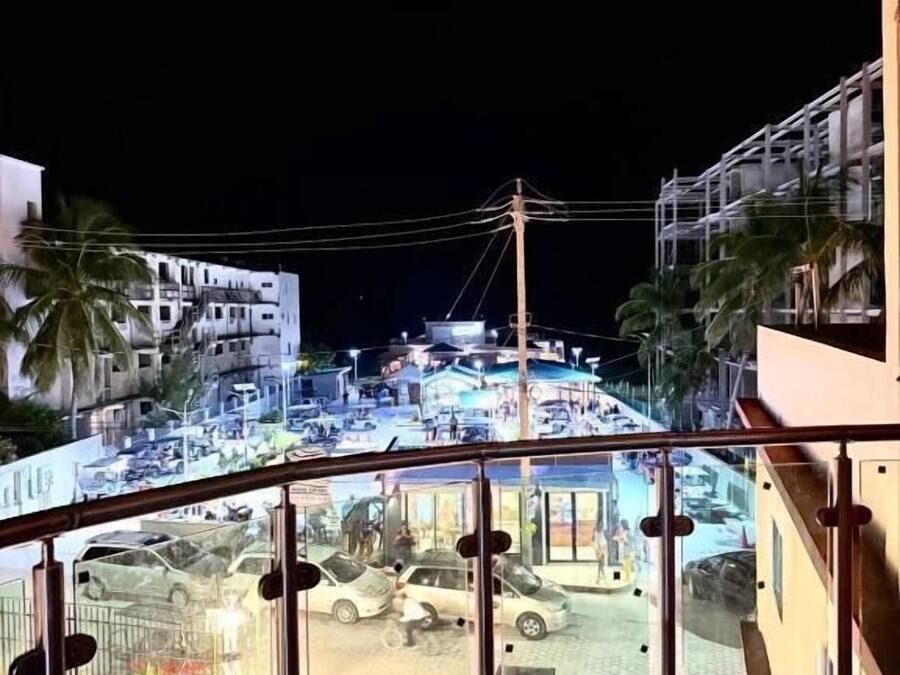 Un balcón con vista a una calle concurrida de noche, que incluye coches estacionados y edificios.