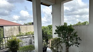 Un balcon abrité, agrémenté de plantes en pot, de piliers en béton et offrant une vue sur un bâtiment aux toits rouges en arrière-plan.
