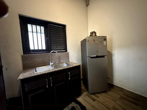 Una cocina compacta con refrigerador de acero inoxidable, un lavamanos con grifo y una ventana con persianas.
