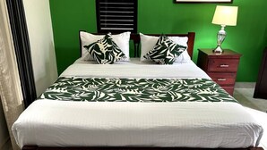 Un lit avec une couvre-lit à motifs blancs et verts, une tête de lit en bois et une table de chevet avec une lampe.