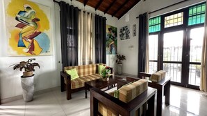 Un salon spacieux avec un plafond haut, un ensemble de canapés, une table basse et de grandes fenêtres avec des rideaux.