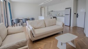 Ein modernes Wohnzimmer mit einem beigefarbenen Sofa, einem kleinen weißen Tisch und einem Essbereich mit Tisch und Stühlen.