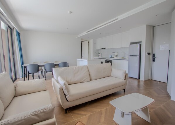 A modern living room with a beige sofa, a small white table, and a dining area with a table and chairs. - 189/267 3BR BEACHFRONT Pool View (Choeng Thale)