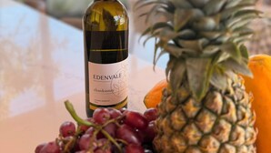 Uma garrafa de chardonnay Edenvale, uma abacaxi e uvas sobre uma mesa.