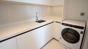 Uma cozinha compacta com máquina de lavar embutida, armários brancos e uma pia de aço inoxidável.