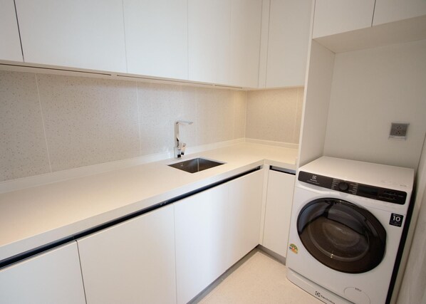 Een compacte keuken met een ingebouwde wasmachine, witte kasten en een roestvrijstalen spoelbak.