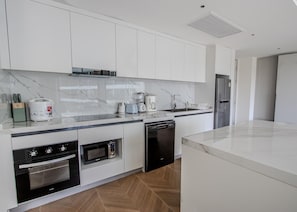 Eine moderne Küche mit weißen Schränken, einer Marmorarbeitsplatte, einem eingebauten Backofen, einem Geschirrspüler und einem Kühlschrank.