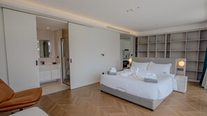 Quarto moderno com cama grande, mesa de cabeceira, criadeira e estante embutida.