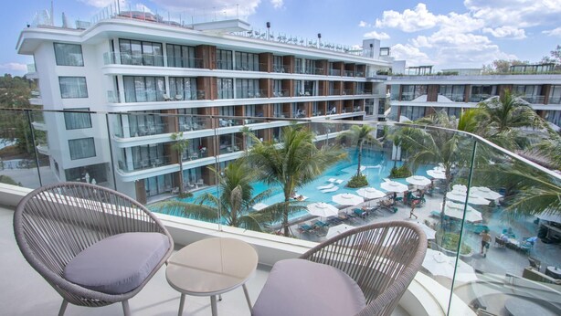 Ein Hotelbalkon mit Korbstühlen, einem Pool und Blick auf die mehreren Stockwerke und Balkone des Gebäudes.